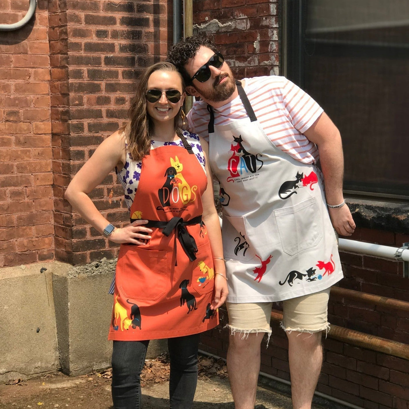White cat apron with “CATS” logo and all-over cat illustrations, front bib style