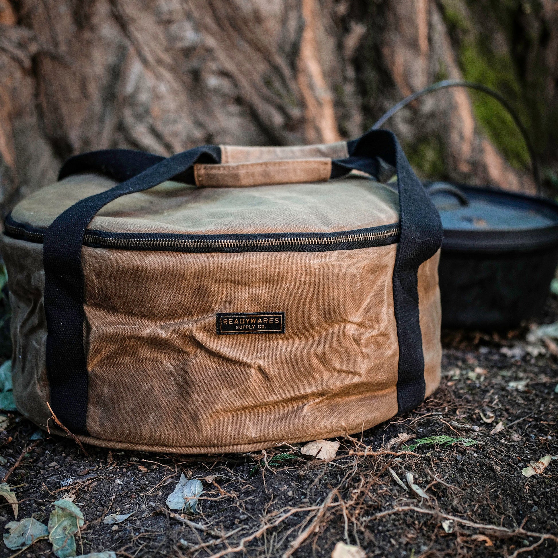 Insulated Dutch oven cover with tan fabric and black side handles, shown outdoors
