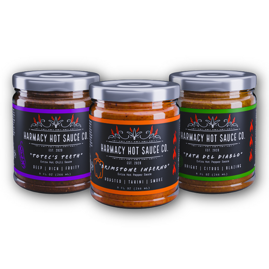 Three hot sauce jars with Harmacy Hot Sauce Co. labels: purple, orange, green