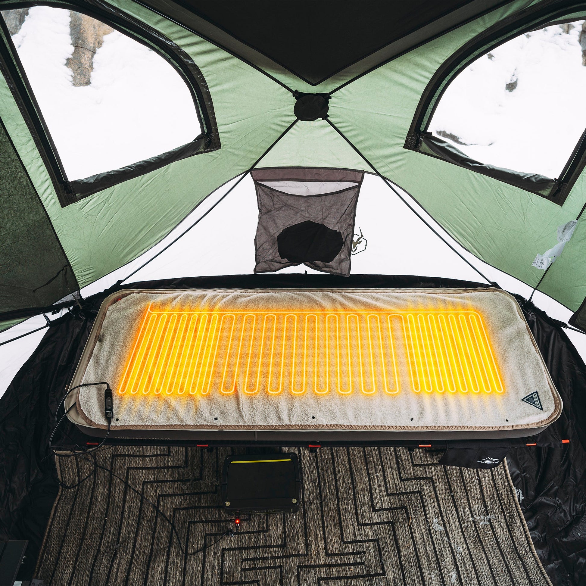 Heated fleece bed cover with glowing heating lines laid over a cot in an outdoor tent