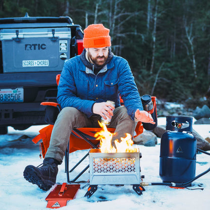 Black insulated growler bag on snowy camp setup beside a gas canister and fire pit.