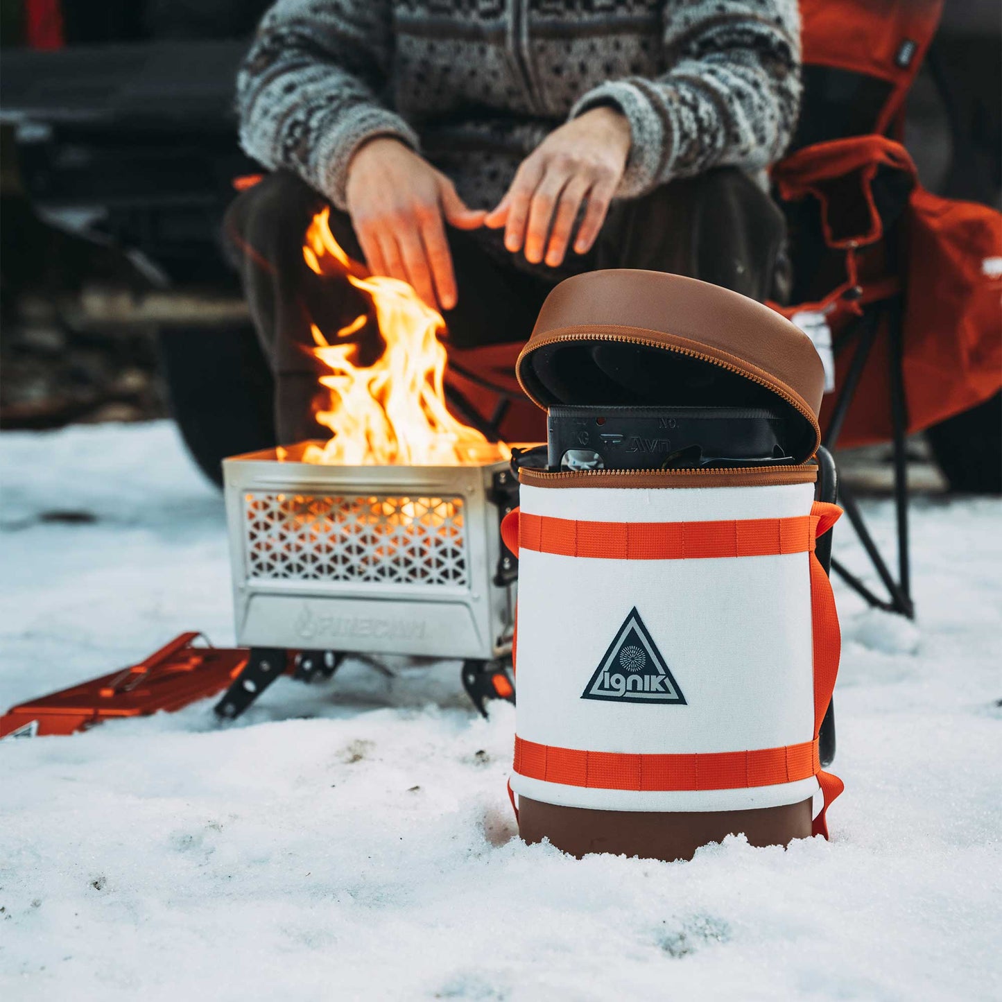 Gas growler with white-and-orange insulated case, open lid, in snowy campsite