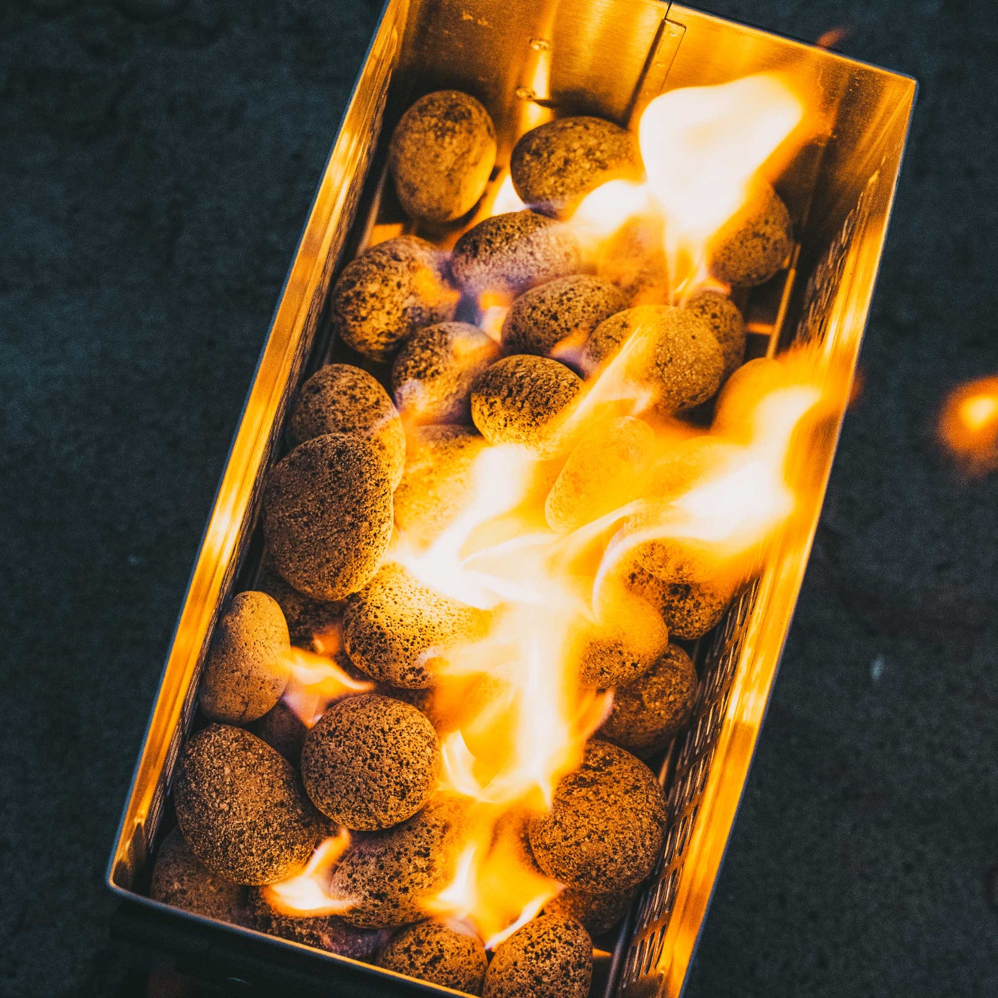 Orange fire pit burner with flames visible inside the steel mesh