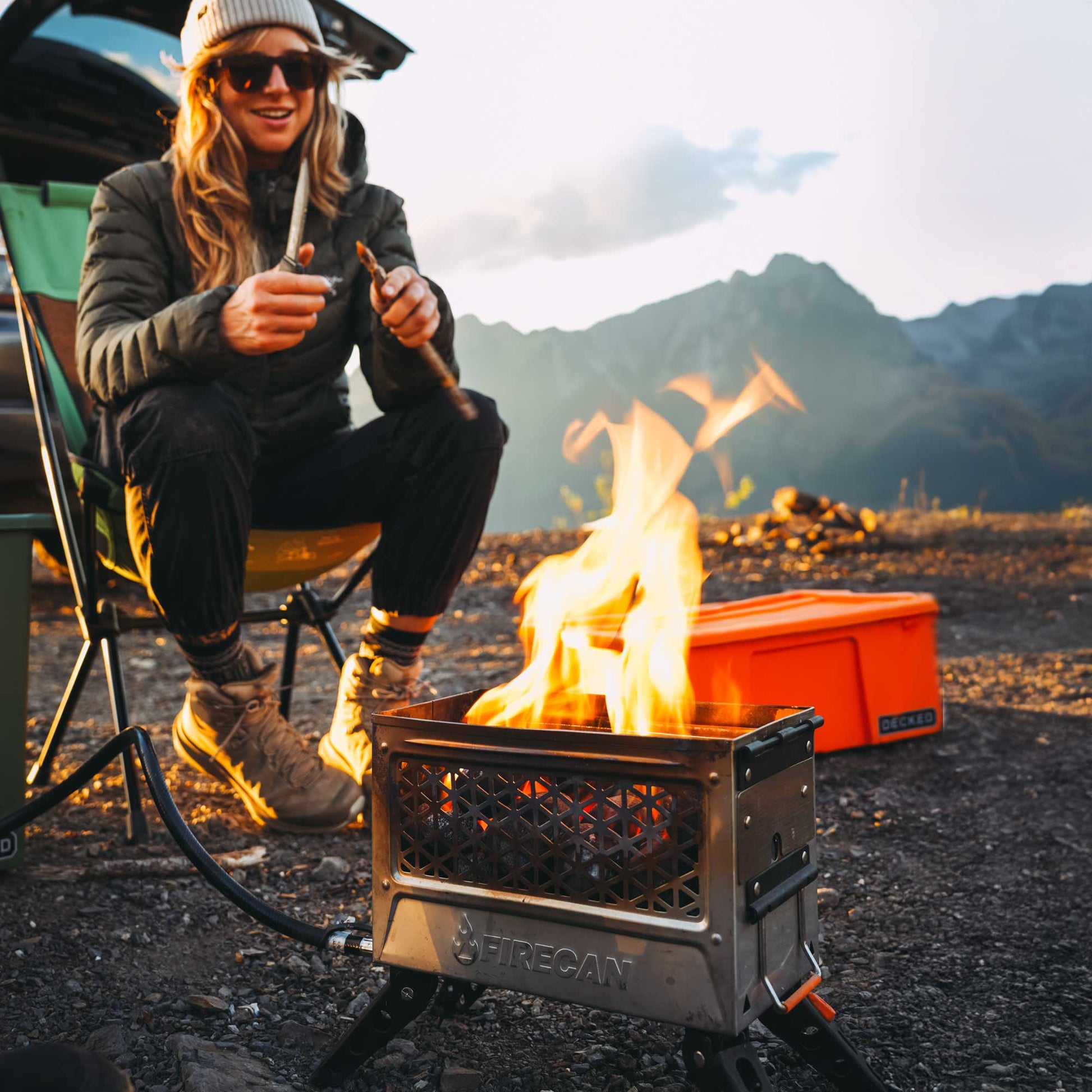 Orange portable fire pit with steel mesh front, active flames, folding legs