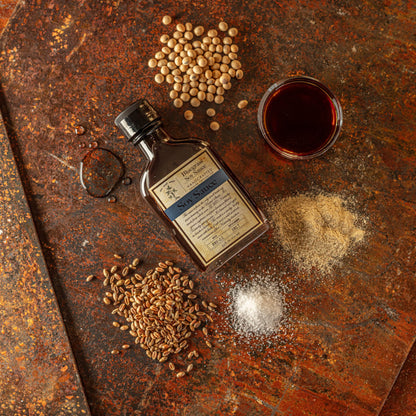 Soy sauce bottle on board with scattered soybeans and grains; label facing up