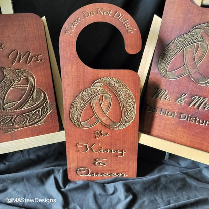 Wooden door hangers with engraved designs and text on a dark fabric background.