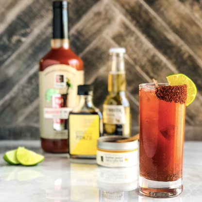 Bloody Mary cocktail glass with ice cubes and red-orange mix, bottles behind