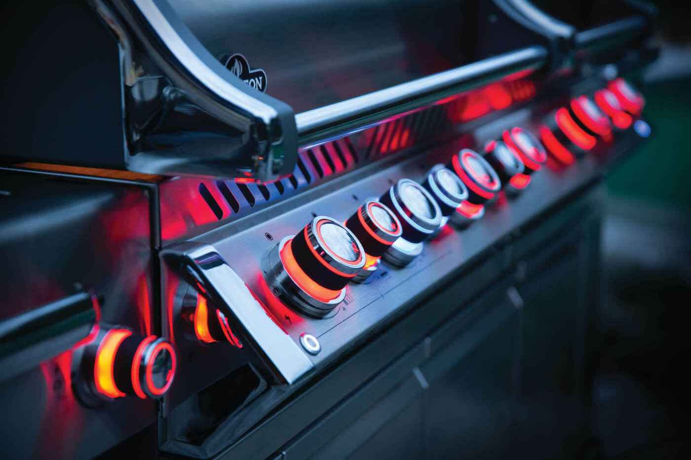 Gas grill burner close-up with glowing red heating elements and row of control knobs