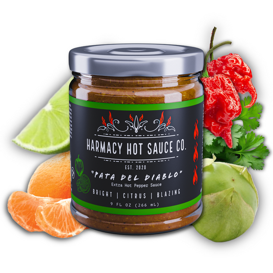 Hot sauce jar with dark label and metal lid, next to lime and chili peppers