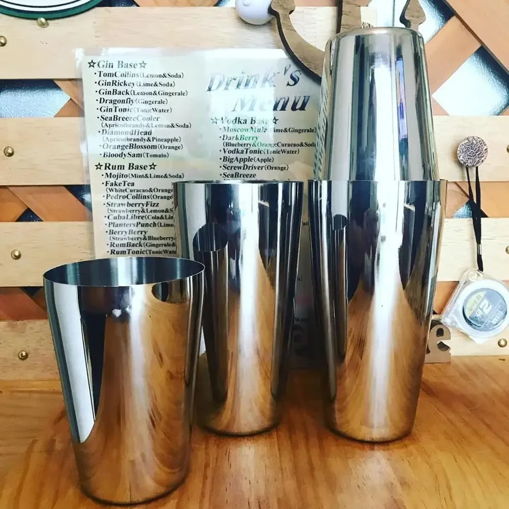 Stainless cocktail shaker set with multiple metal cups on a bar rail