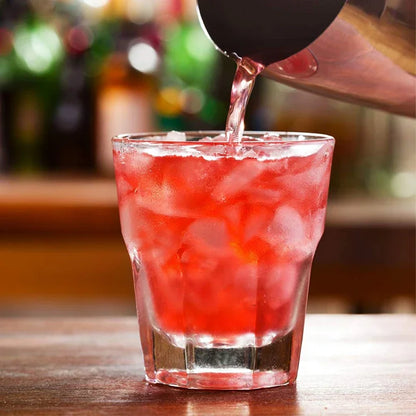 Stainless shaker pouring into a red cocktail with ice in a rocks glass