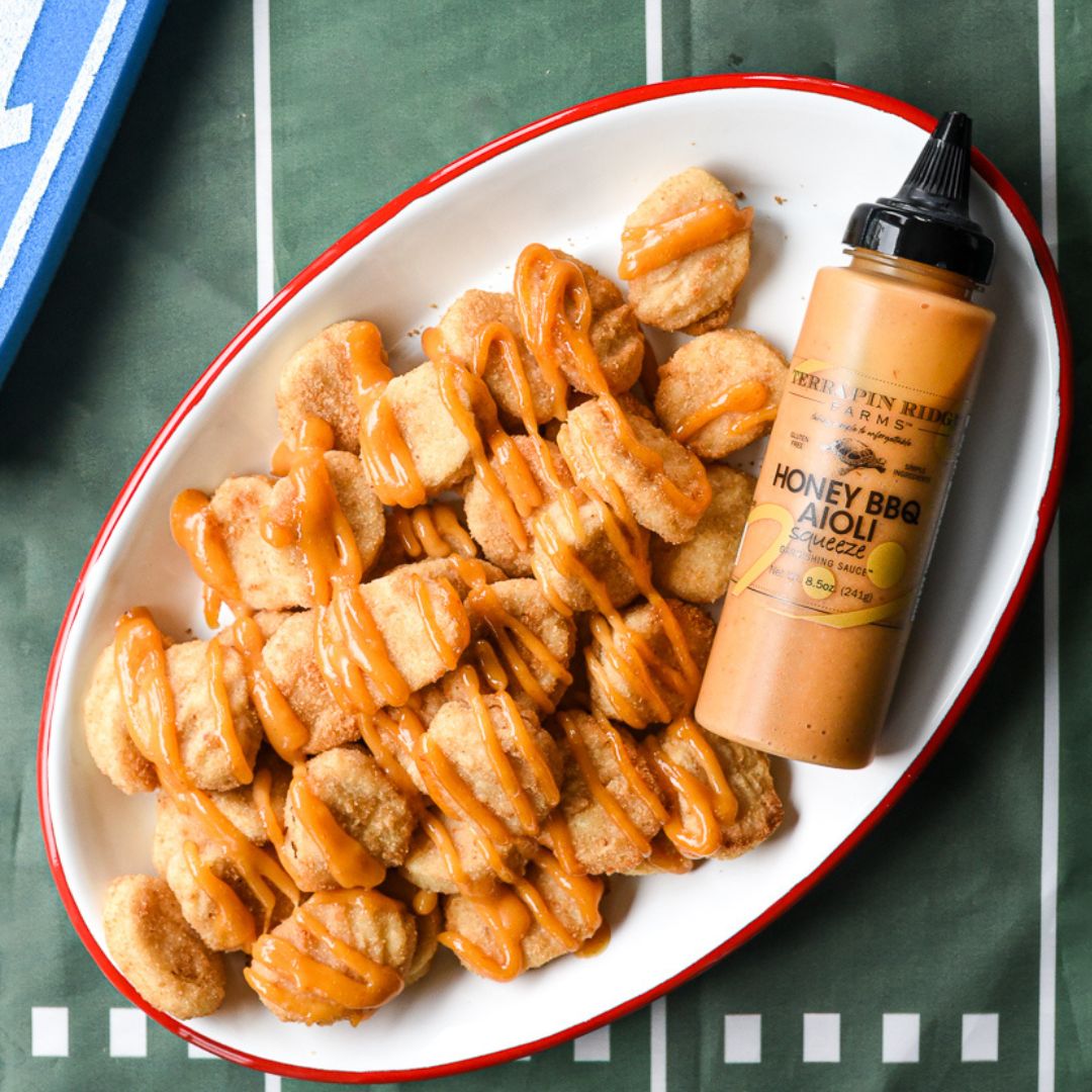 Honey BBQ aioli squeeze bottle beside seasoned chicken and fries in white bowl