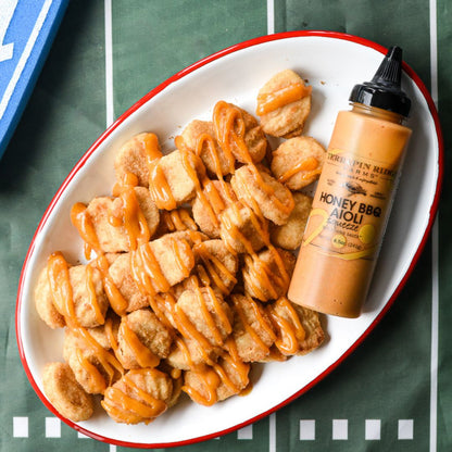 Honey BBQ aioli squeeze bottle beside seasoned chicken and fries in white bowl