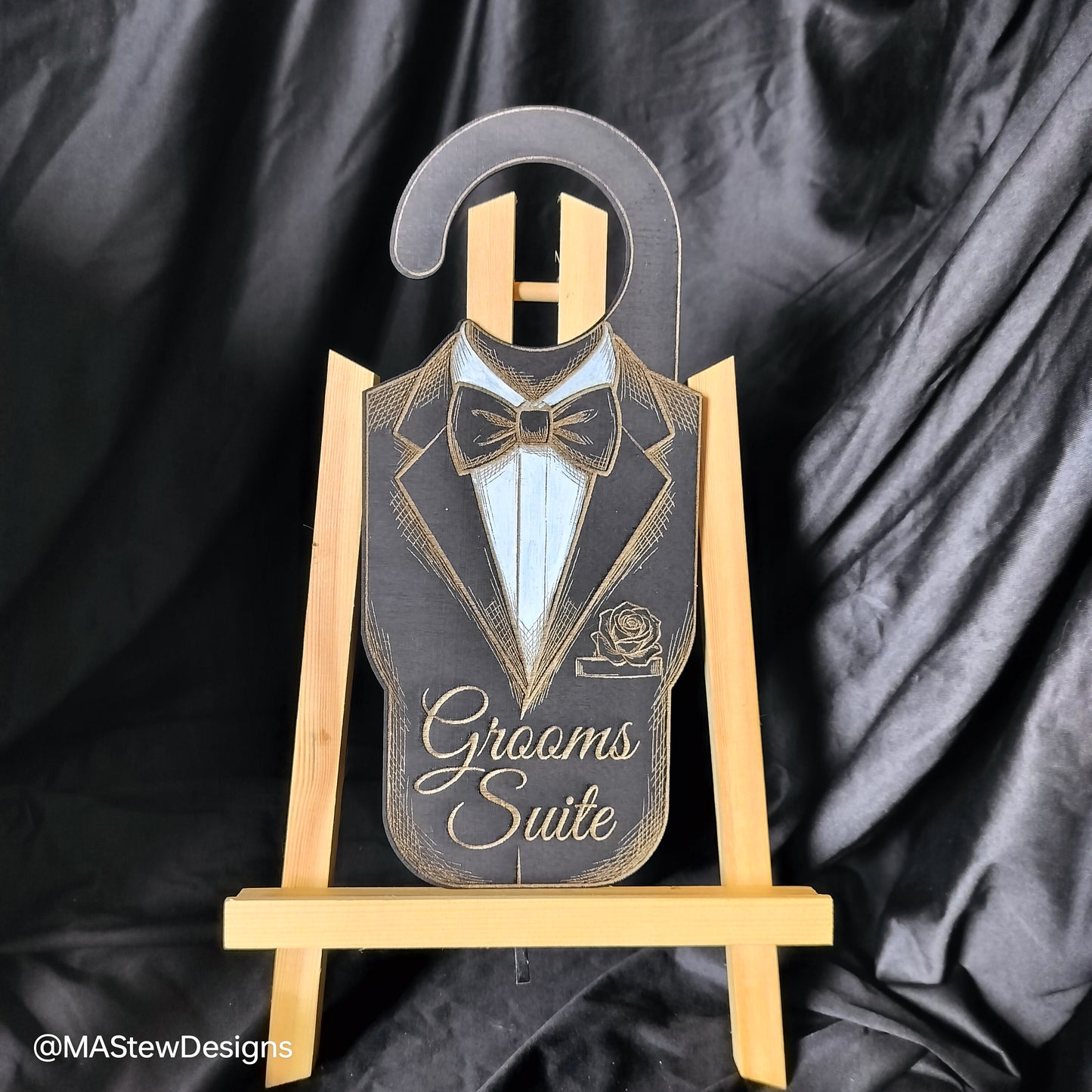 Decorative sign with tuxedo design on a wooden stand against a black satin background