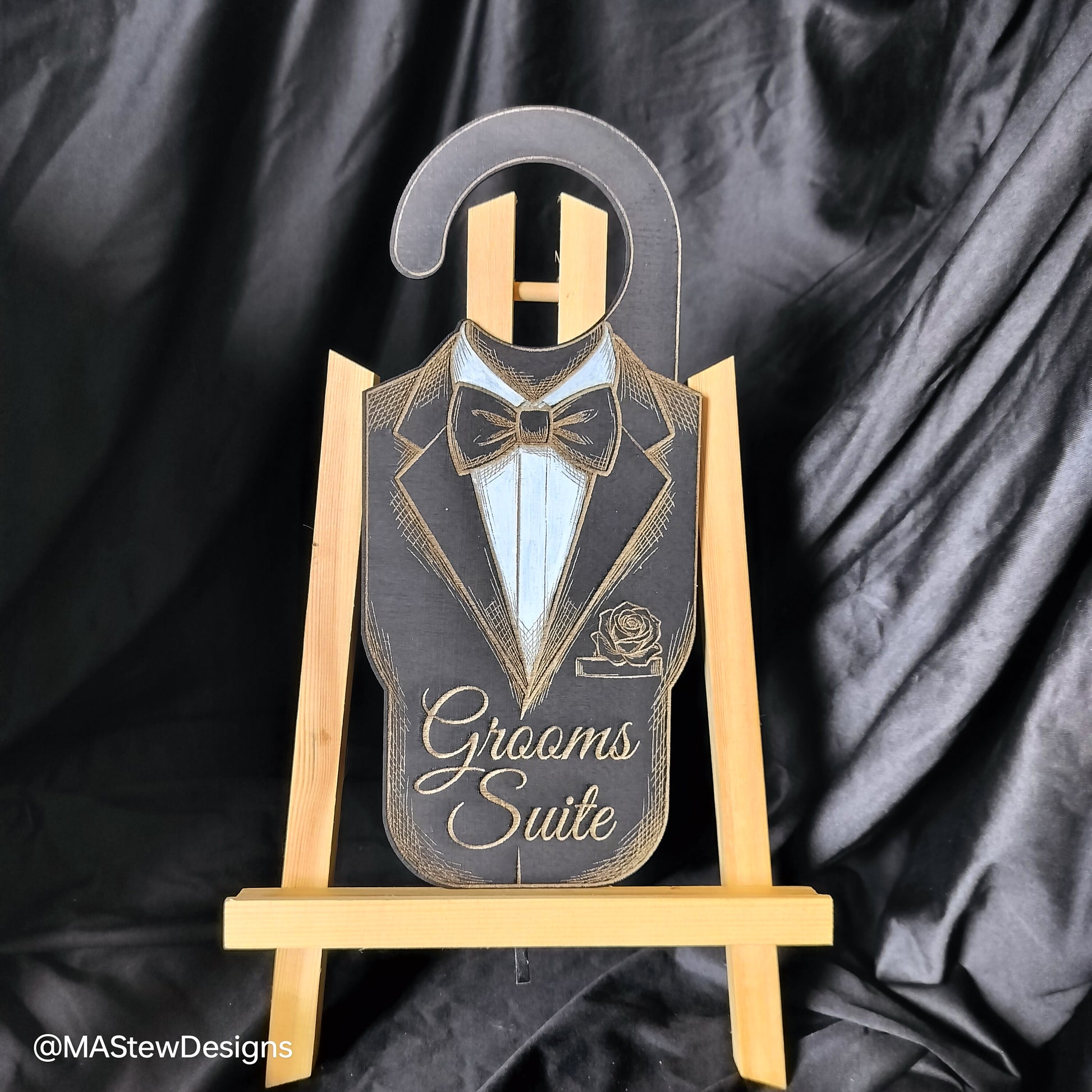 Decorative sign with tuxedo design on a wooden stand against a black satin background