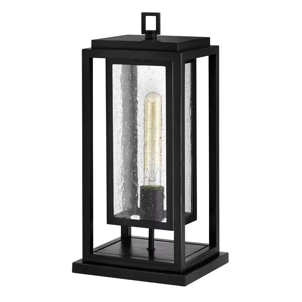 Black outdoor wall lantern with single clear glass panel and glowing bulb inside