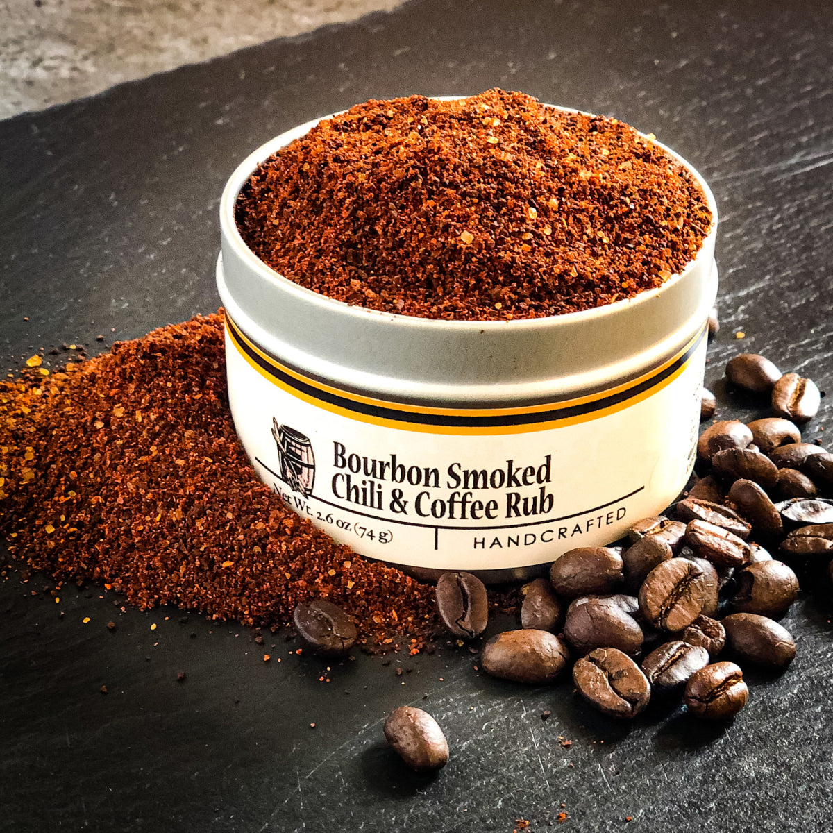 Round jar of chili and coffee rub with coffee beans beside, red-brown ground spice