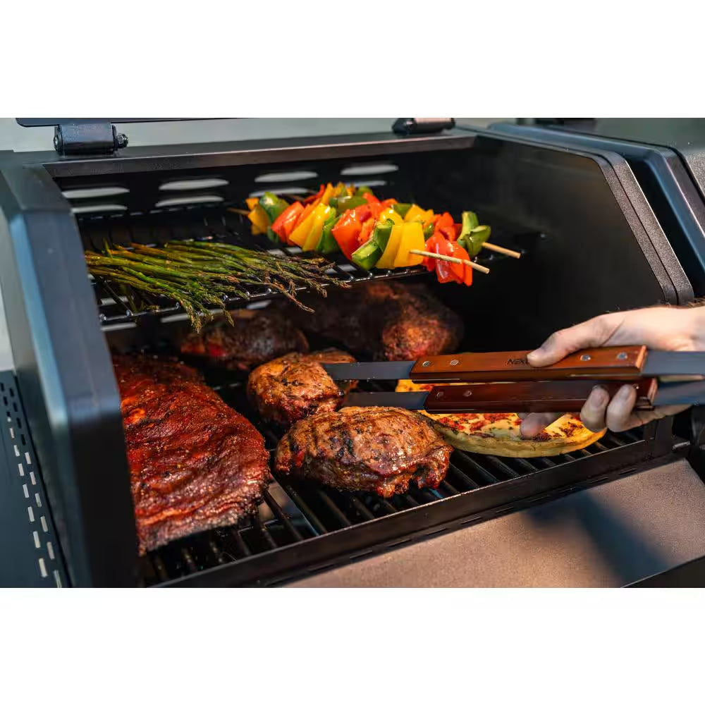 Open gas grill with cooked meat on grates and skewered vegetables above