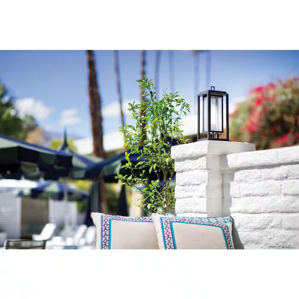 Black outdoor lantern on stone wall near patio seating and plants