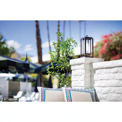 Black outdoor lantern on stone wall near patio seating and plants
