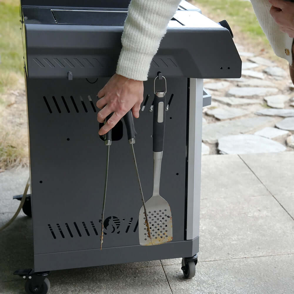 Stainless gas grill with side handle and grilling tools hanging from hooks