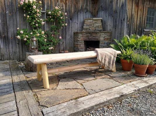 Handmade solid wooden bench, light wood seat with two legs, beige throw draped on backrest.