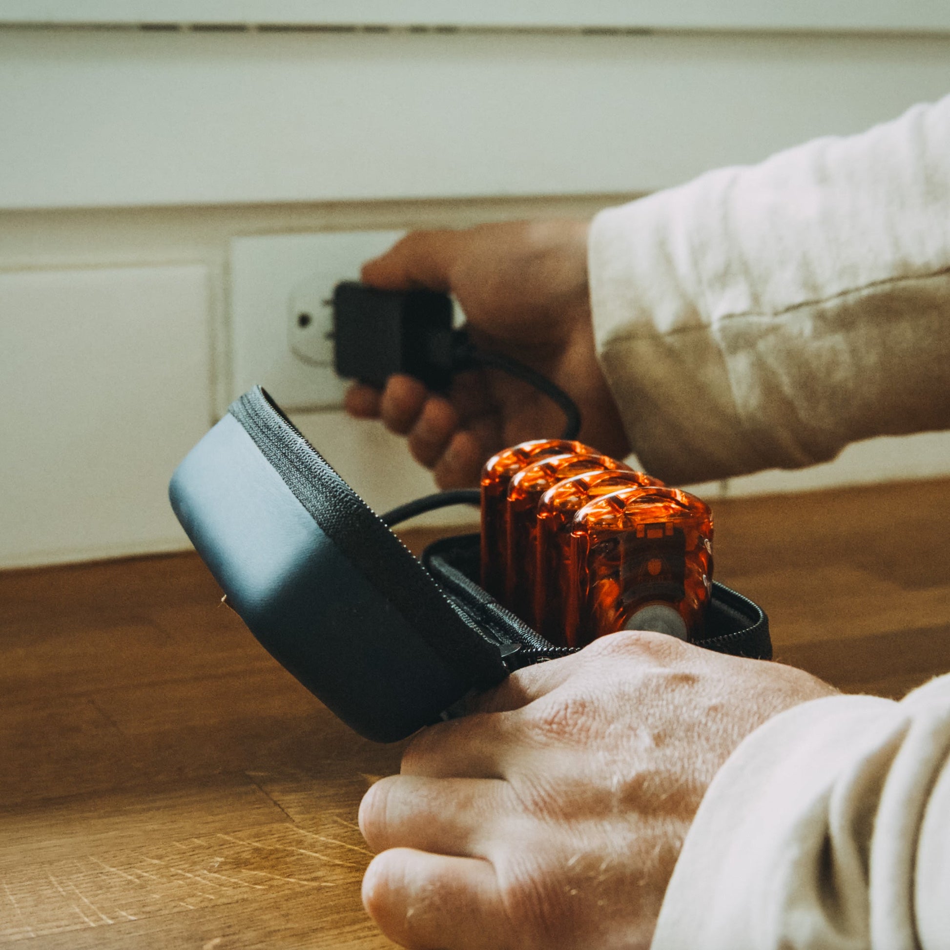 Rechargeable hand warmer in amber orange with strap, held in hands