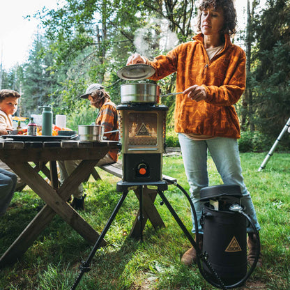 Outdoor heater stove on tripod with pot on top and side accessory container