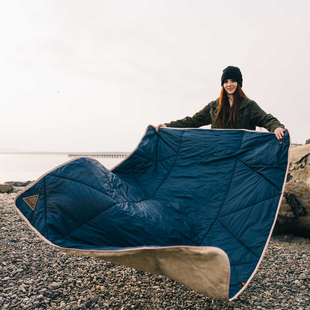 Blue heated blanket spread outdoors with tan edge trim and attached power cable
