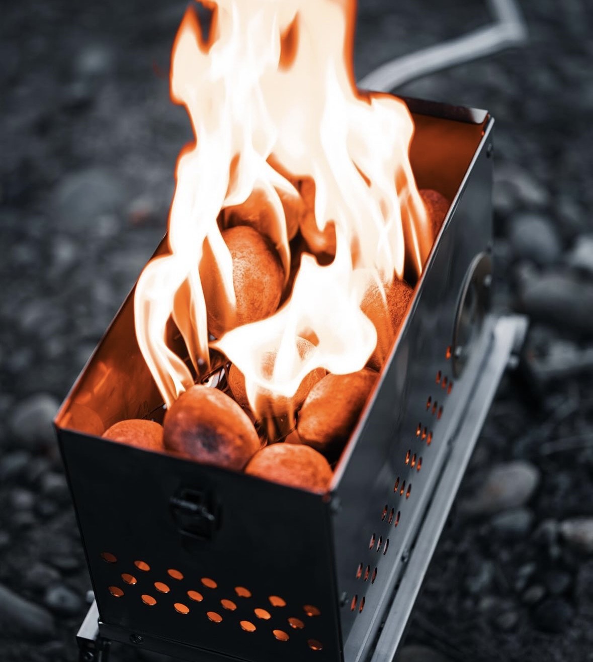 Open campfire firebox filled with burning logs and orange flames over gravel