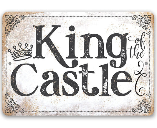 Rectangular metal sign with bold black “King of the Castle” text and crown, distressed white