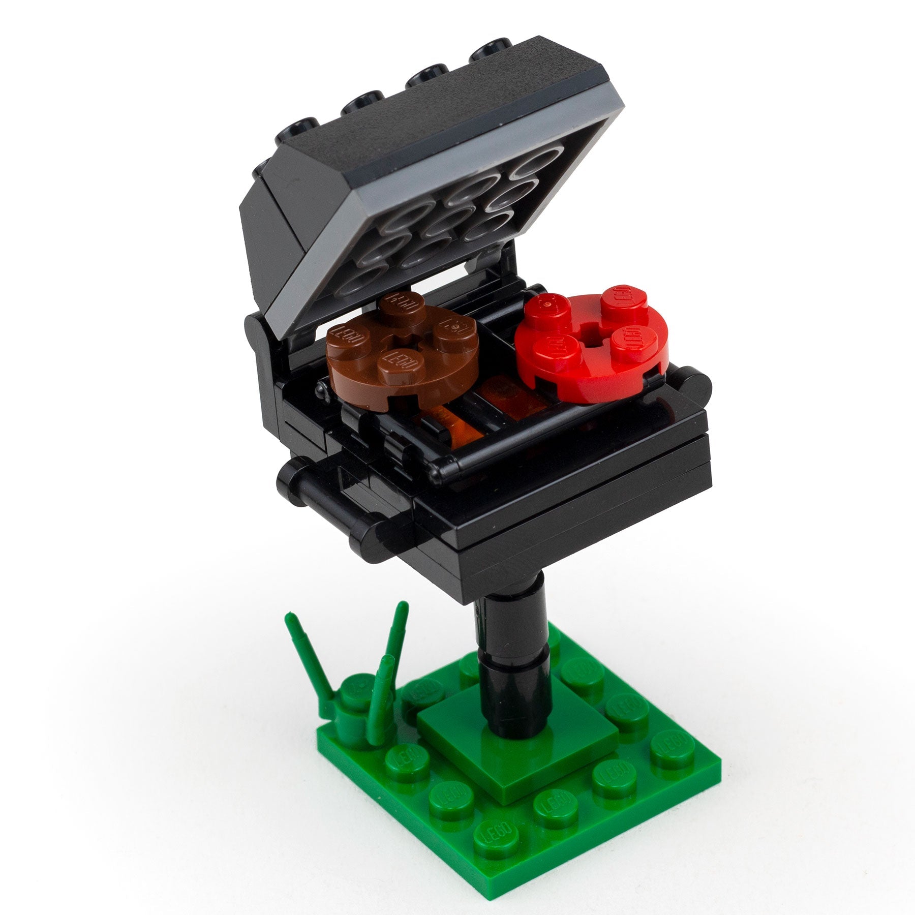 LEGO-compatible BBQ grill set with open lid, brown and red food pieces, on green base