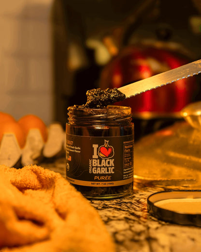 Black garlic purée jar with dark paste on top, spoon resting on the jar