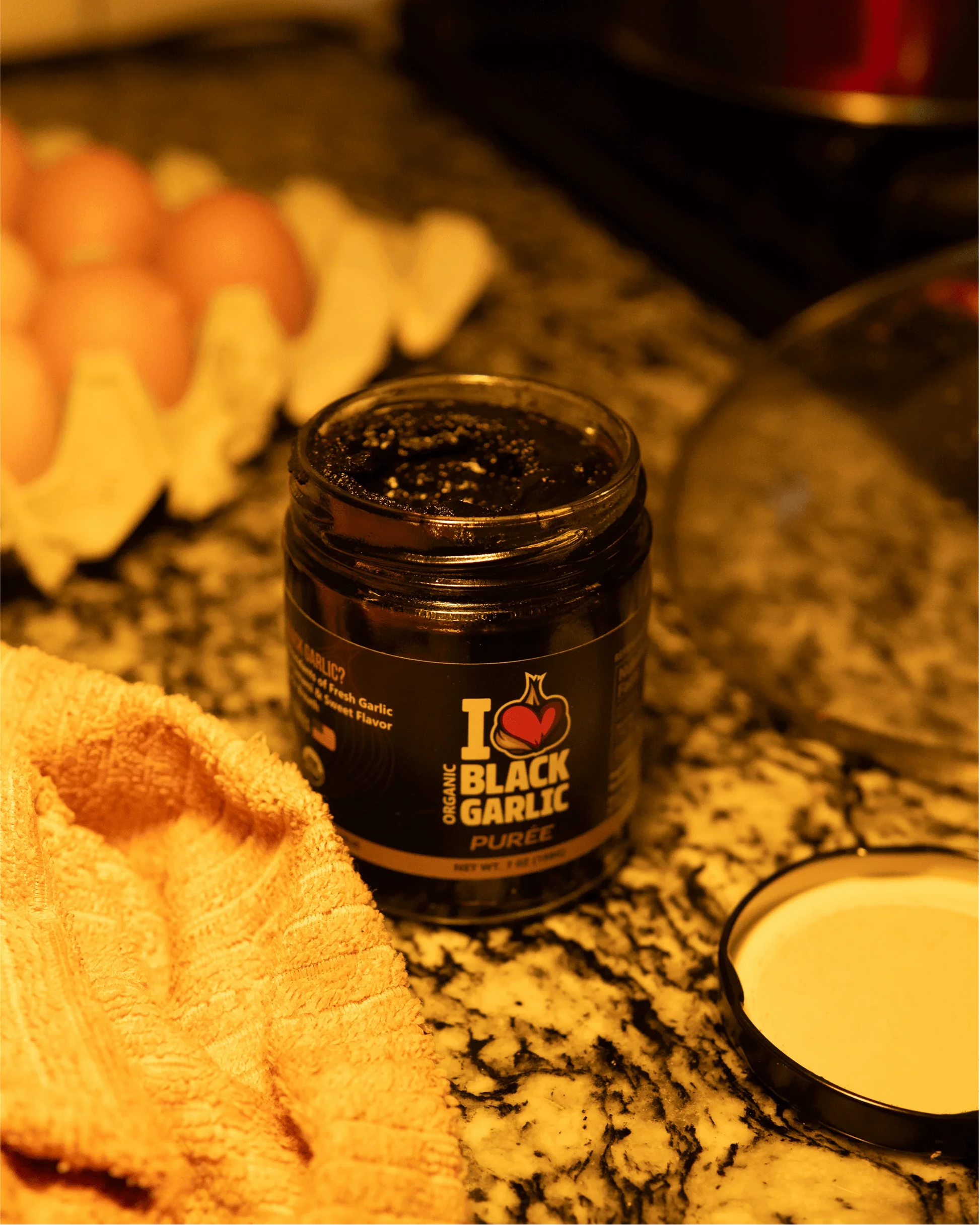 Black garlic purée jar with black lid on countertop; dark paste visible through glass