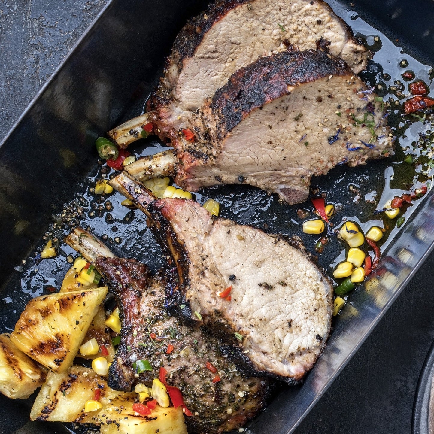 Spice-rubbed pork steaks on a metal tray with peppercorns and herbs