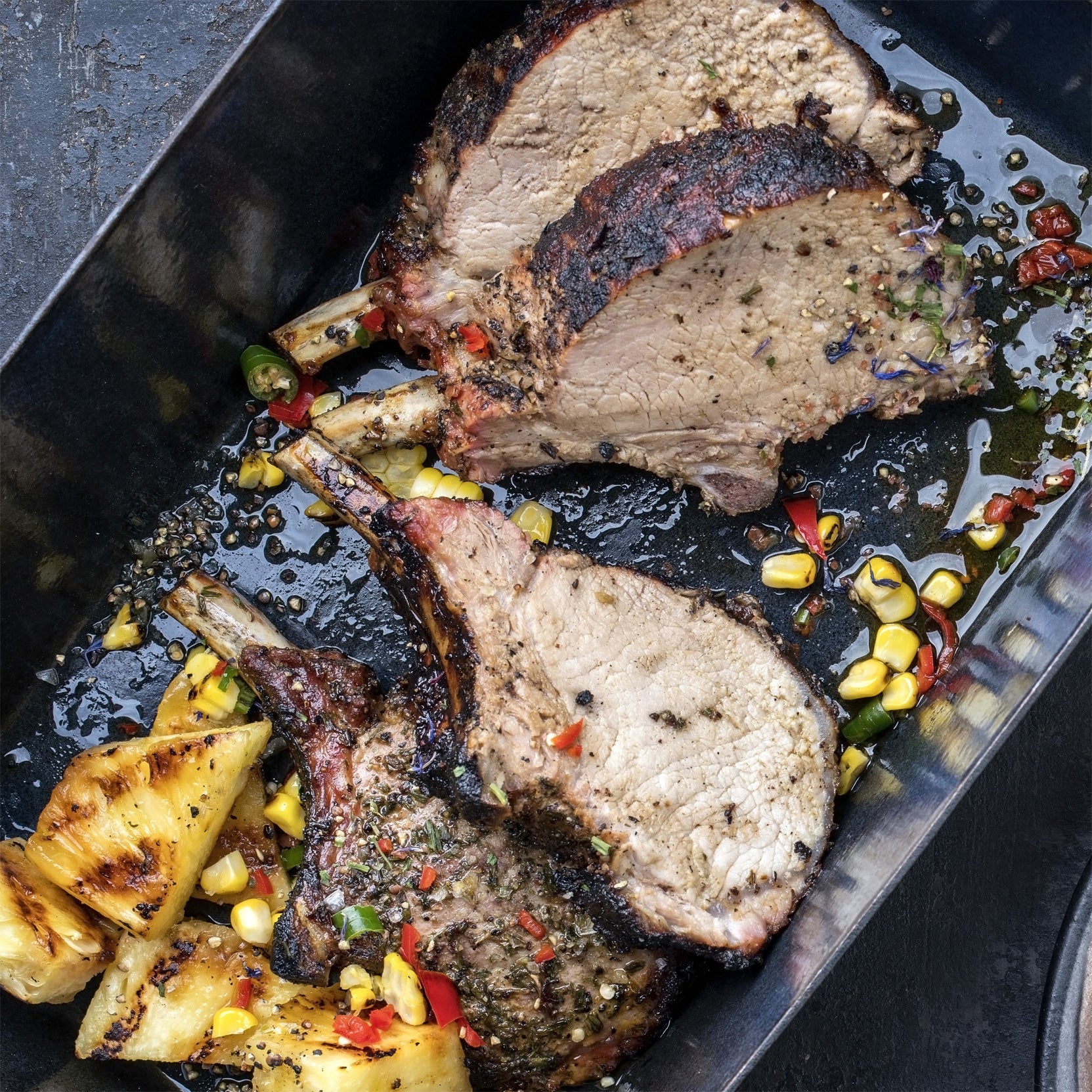Spice-rubbed pork steaks on a metal tray with peppercorns and herbs