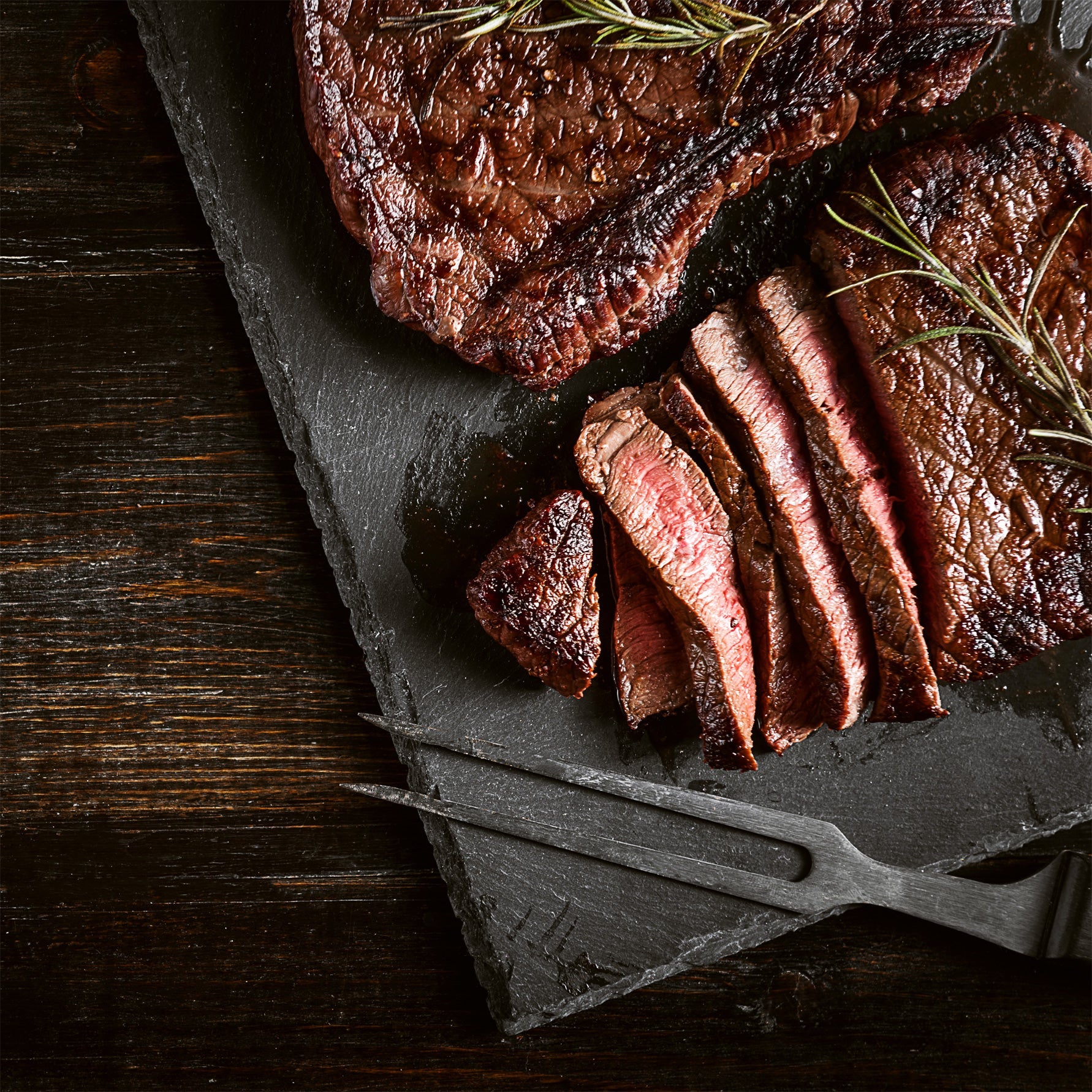 Spice-rubbed pork chops on a dark board with rosemary sprigs